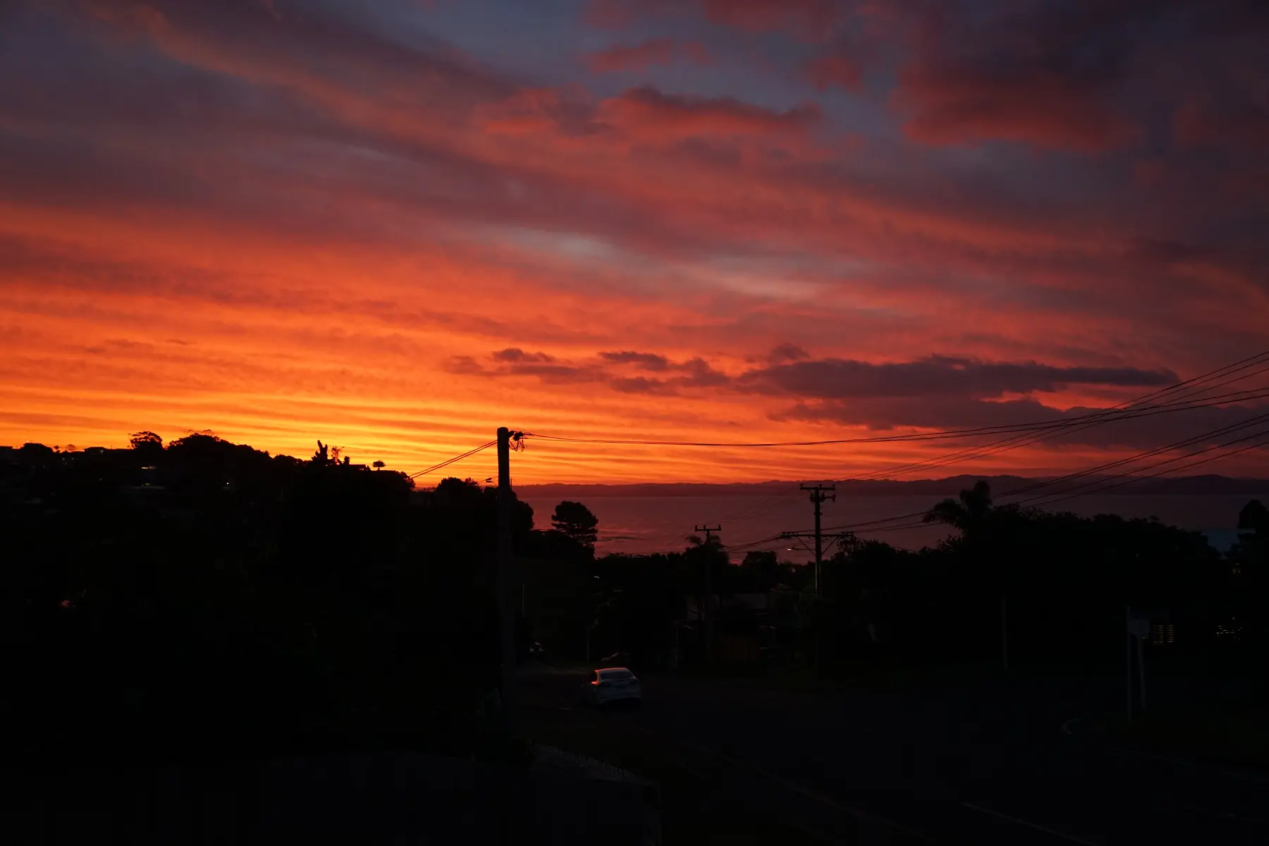 A vivid red sunset above a dark suburban horizon