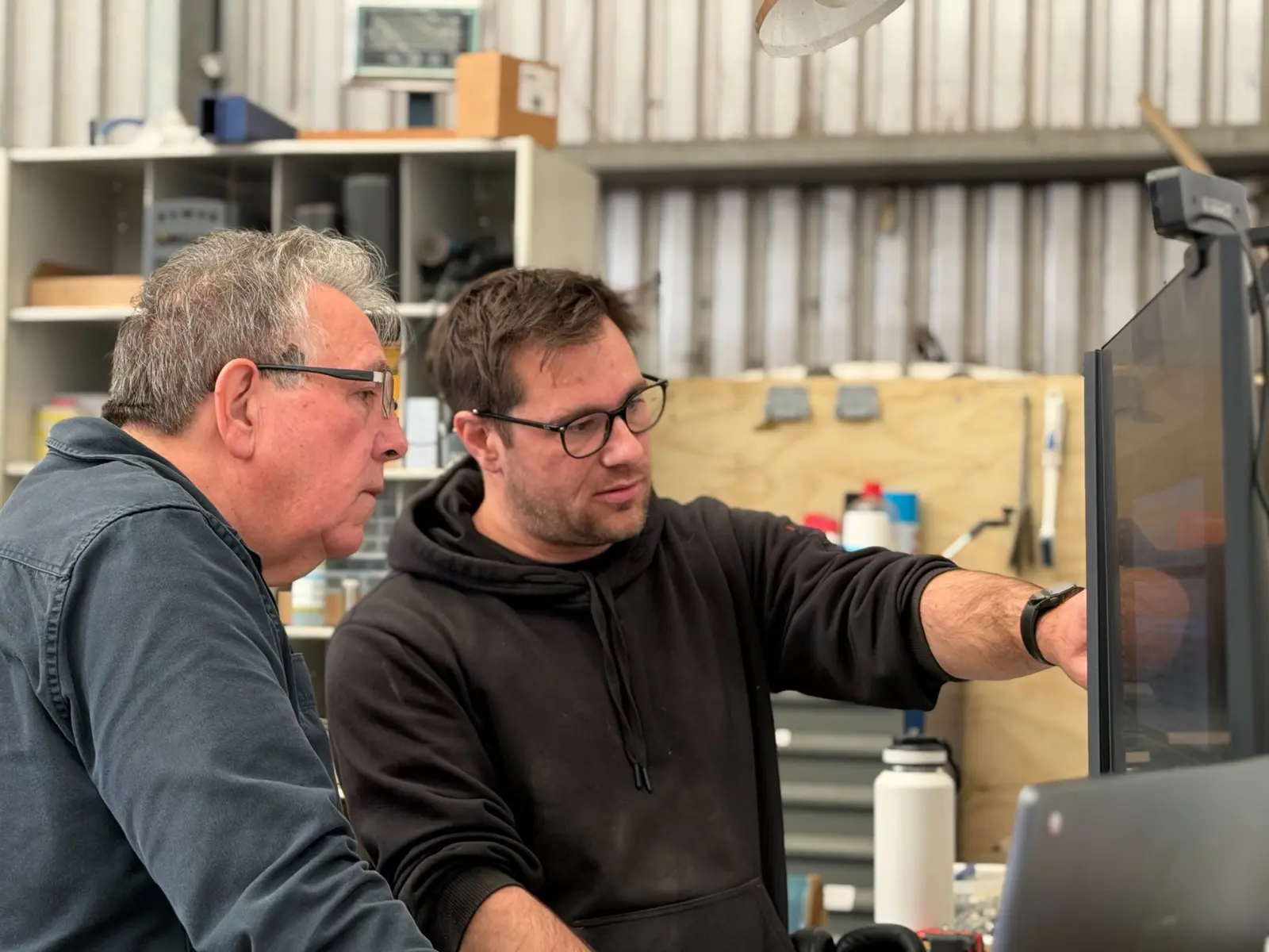 Two people reviewing work at a computer in a machine workshop