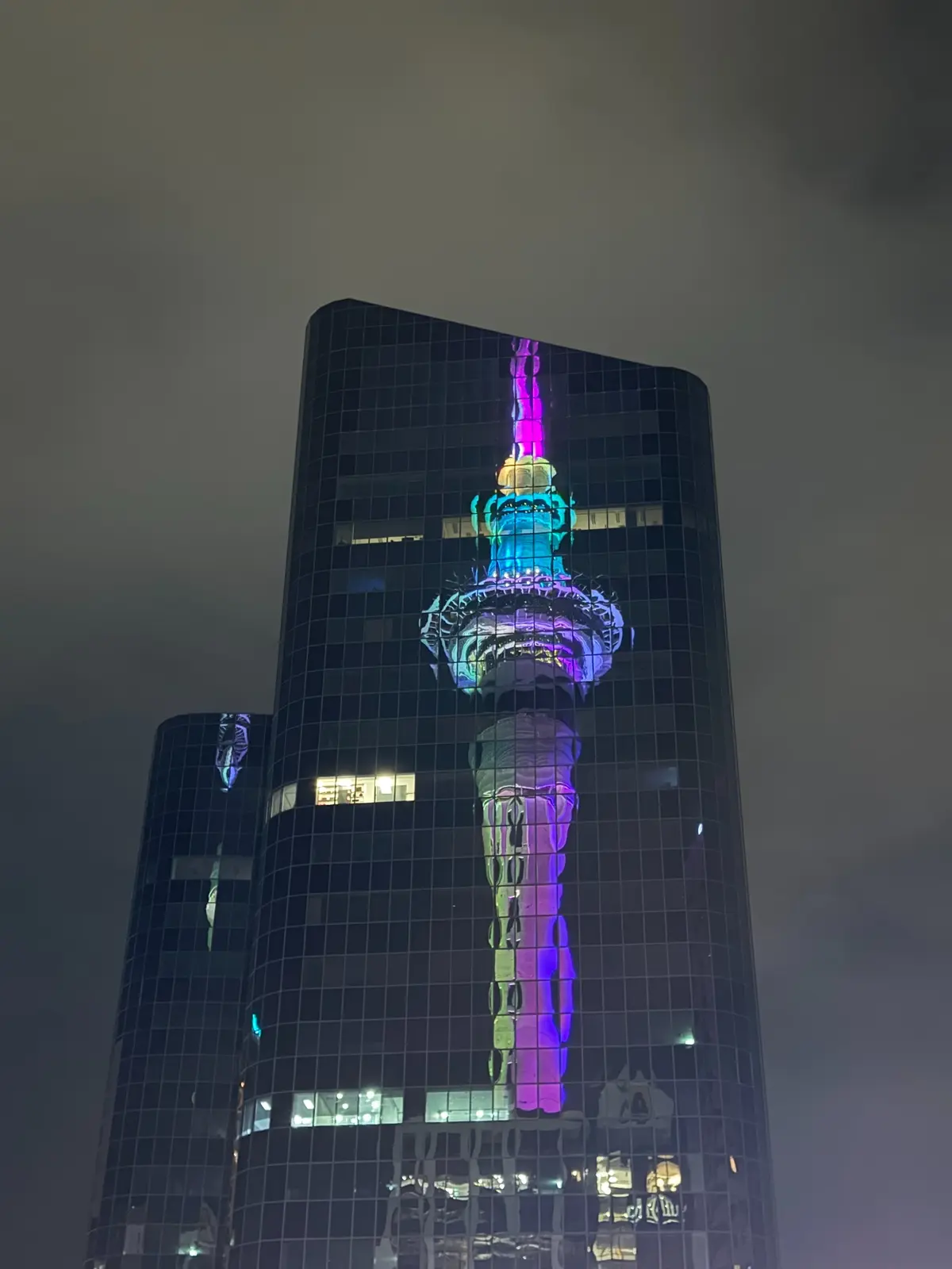A colourful tower projection reflected across a city building at night